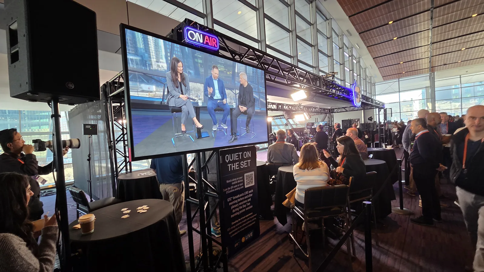 A live broadcast set at a corporate conference with attendees watching from the surrounding space