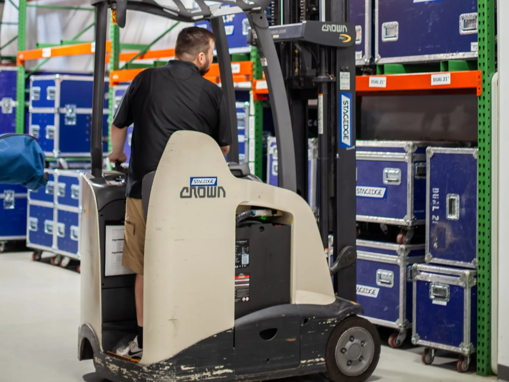 A Stagedge crew member drives a forklift past warehouse racks stacked with blue Stagedge road cases