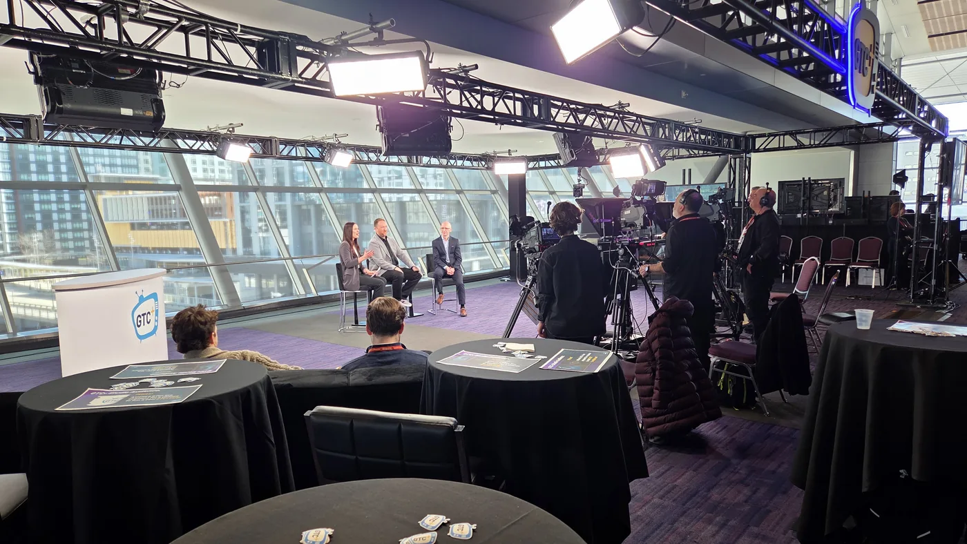 Panel discussion filmed under lighting truss at a conference venue with an audience seated at tables