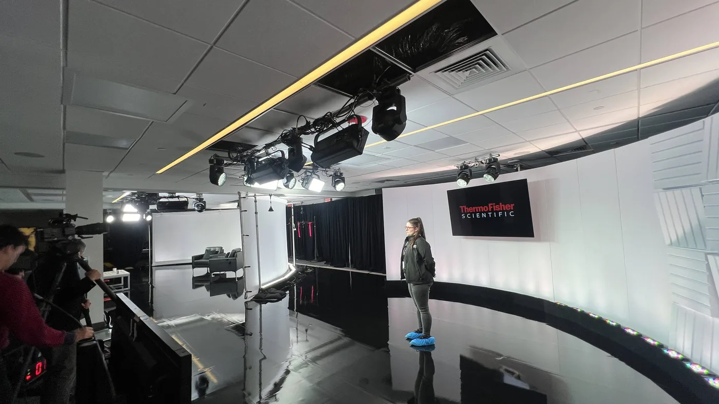 Television studio built inside a corporate office with a gloss floor, lighting truss, and branded wall