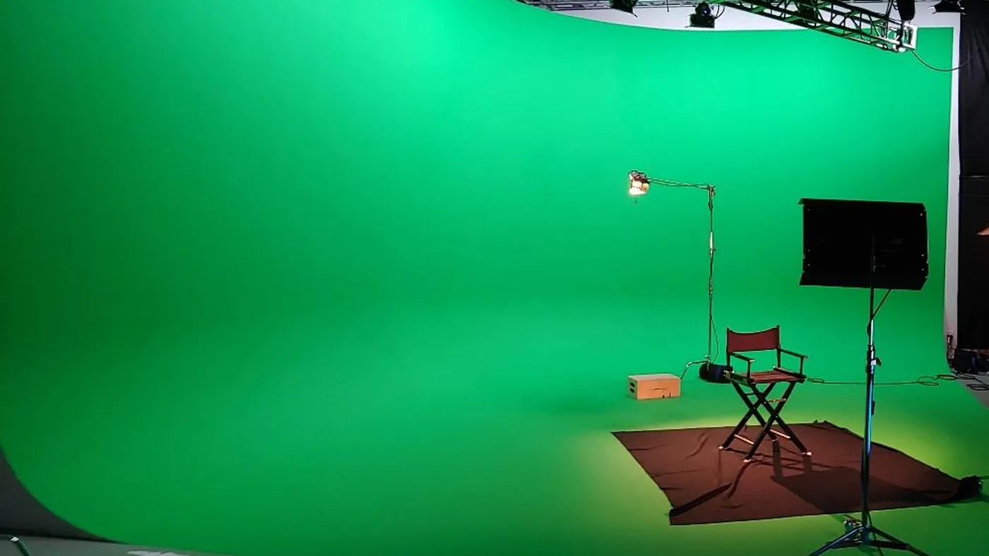 Cyclorama wall painted chroma key green with a director chair and lighting stand on the studio floor