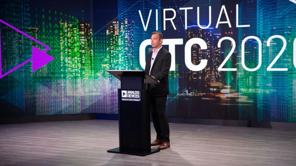 Presenter on stage with large projection screens at the Analog Devices 40th General Technical Conference
