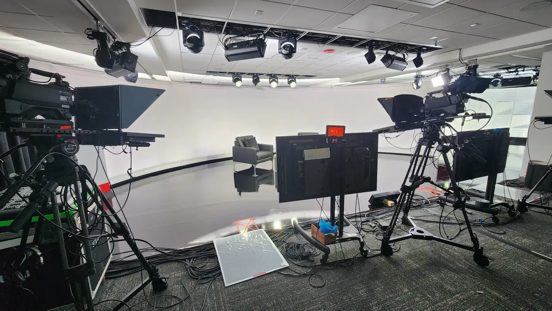 Broadcast studio set with cameras, teleprompters, and stage lighting rigged for a corporate digital meeting